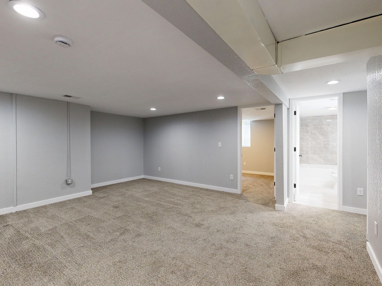 Empty basement room with neutral carpet and recessed lighting.