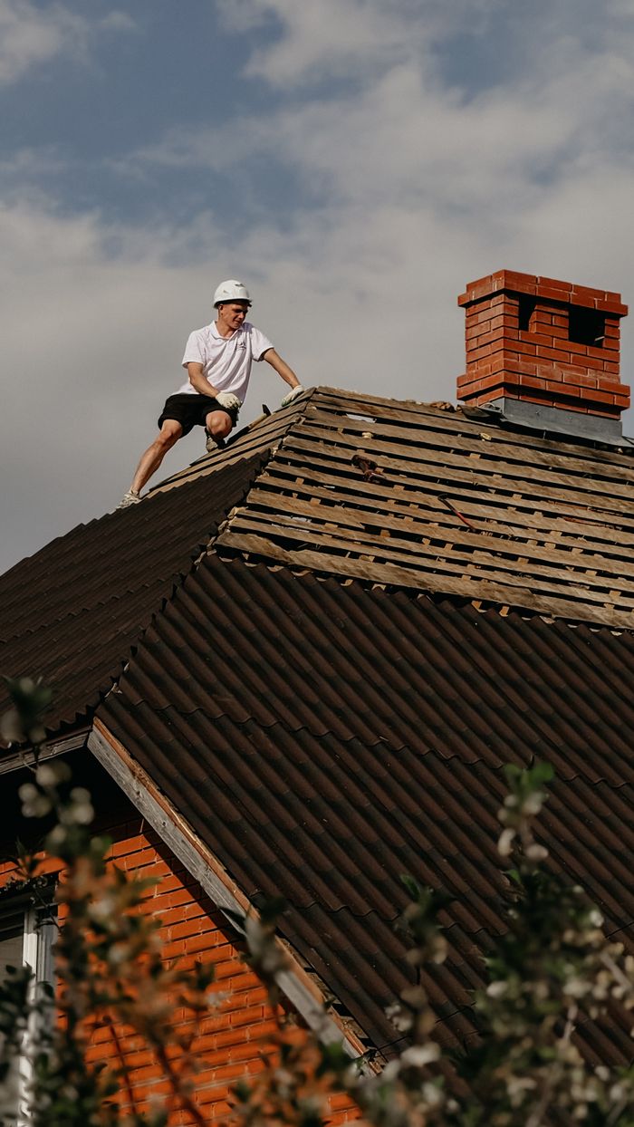 Man in safety helmet repairing roof of red brick house under clear sky.