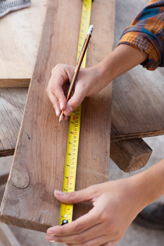 A skilled craftswoman measuring wood with precision in a workshop.